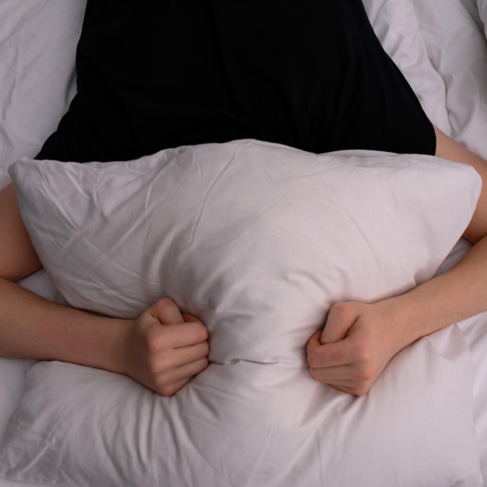 Person with a migrane holding their head beneath a pillow