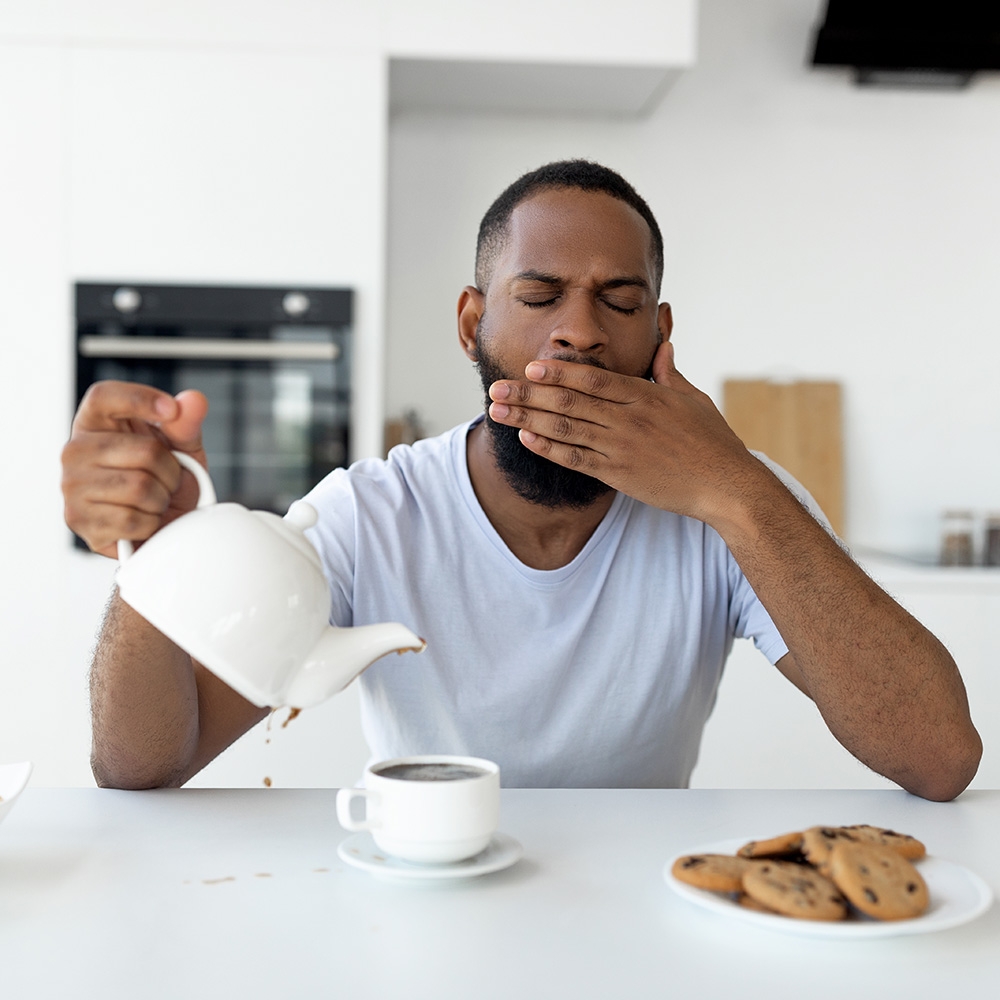 Man yawning and pouring coffee at breakfast