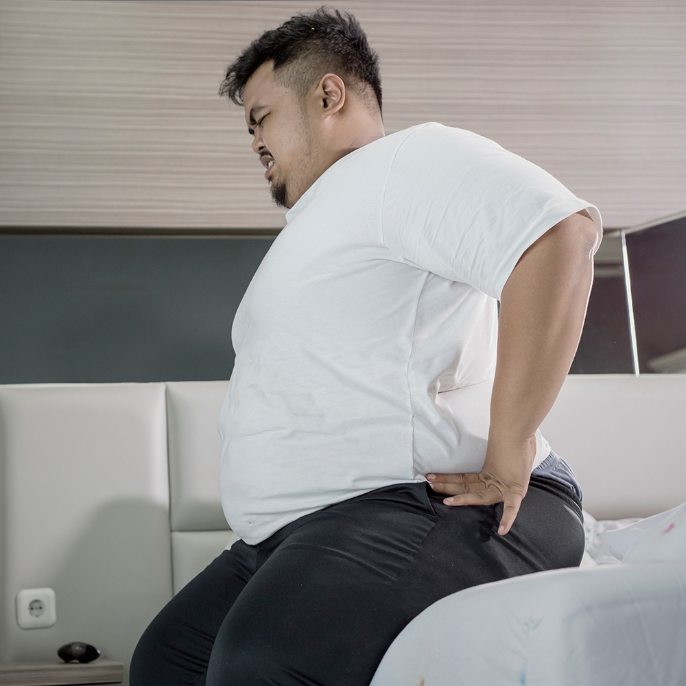 Overweight man with a backache while sitting on the bed